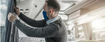 a coach bus driver wearing a mask and fixing curtains on a bus